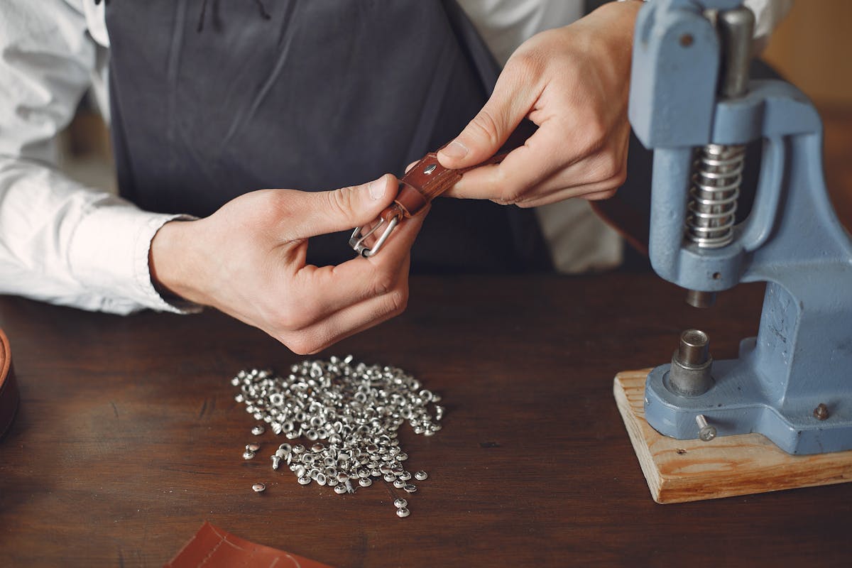Artisan hands setting rivets on a leather belt in a workshop